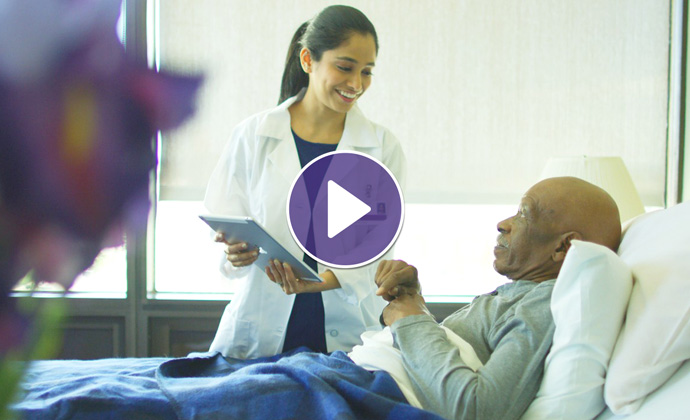 A VITAS physician uses a tablet as she talks with a patient who is in a hospital bed