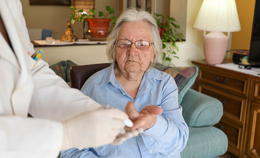 A clinician pricks the finger of an older woman to check her blood sugar