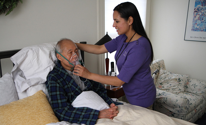 A VITAS team member helps a patient with his oxygen mask as he sits up in bed