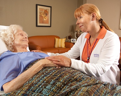 A VITAS nurse comforts a patient in a bed