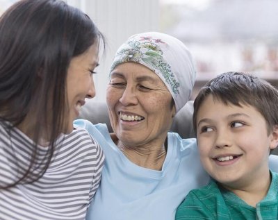 A patient sits on a sofa at home with her daughter and grandson