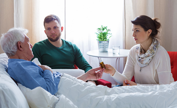 A couple talks to an older man who is lying in bed